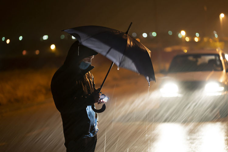 Man with umbrella standing on wet street in city at night