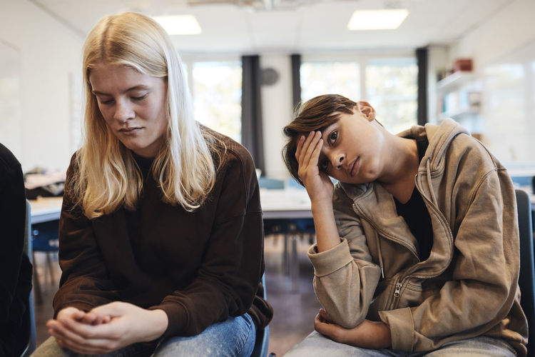 Sad teenage boy sitting by blond girl in classroom during therapy