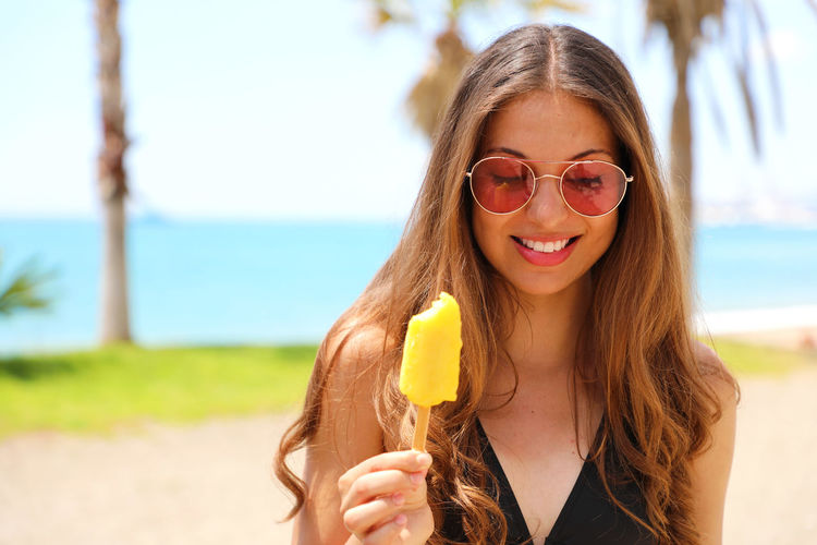 Beautiful woman having popsicle while standing at beach