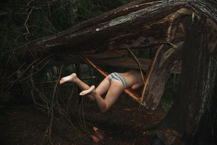 Shirtless woman relaxing on tree trunk in forest