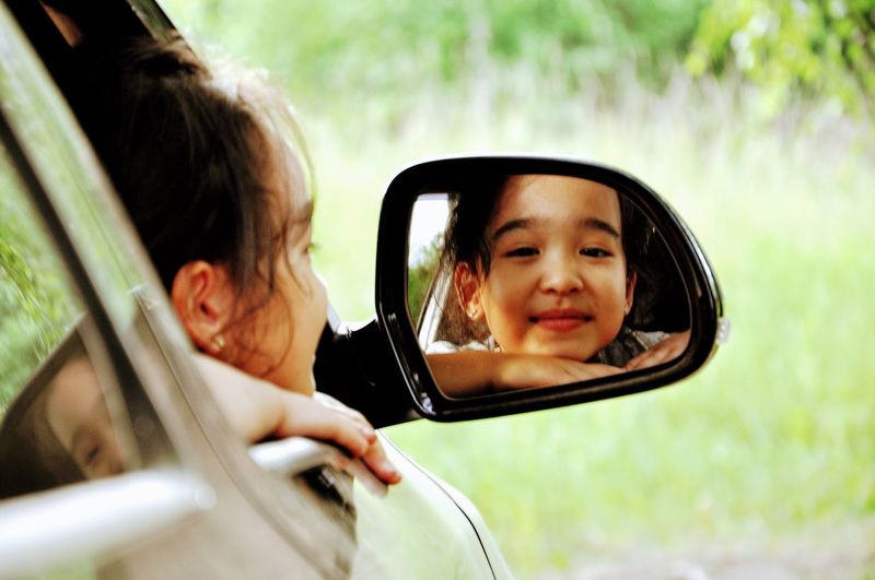 Close-up of girl looking in car mirror