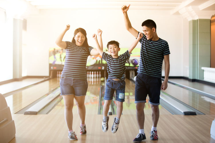 Happy family with arms raised standing on hardwood floor at bowling alley