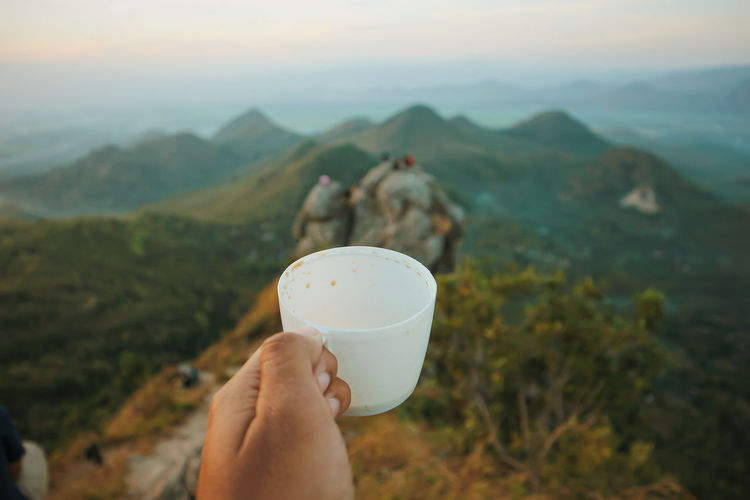 Midsection of person holding ice cream against mountains