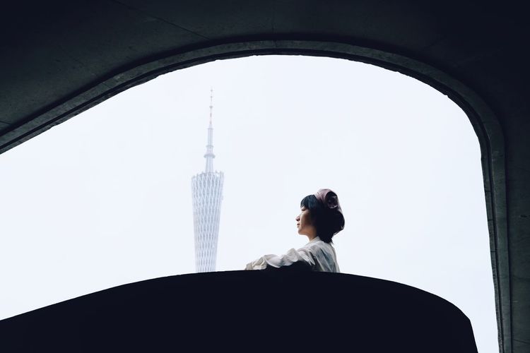 WOMAN STANDING BY BUILDINGS AGAINST SKY