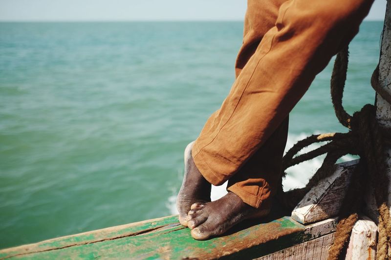 Low section of man standing on boat sailing in sea