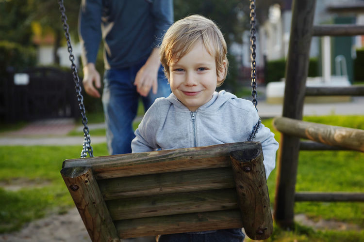 Portrait of smiling boy standing by swing at yard