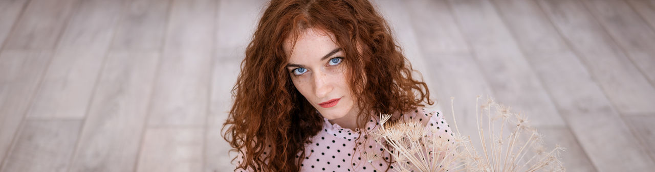  red-haired girl with blue eyes, dressed in a polka-dot blouse, looks at the camera mysteriously