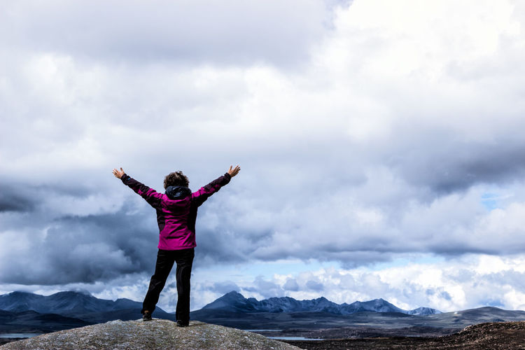 Woman standing on rock against cloudy sky
