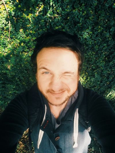 High angle portrait of man taking selfie while blinking against plants
