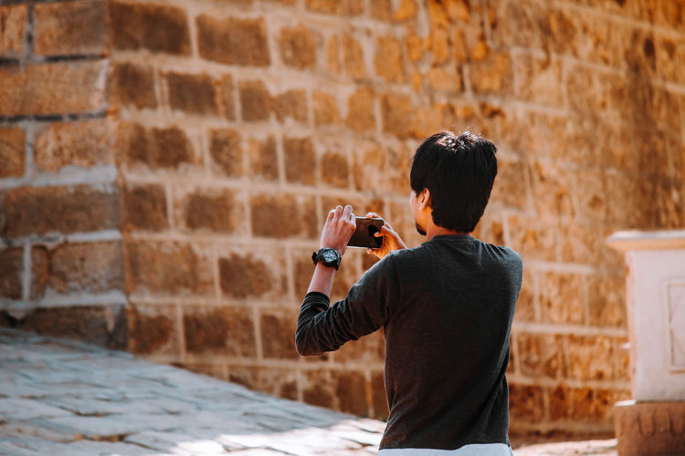Rear view of man photographing while standing against wall