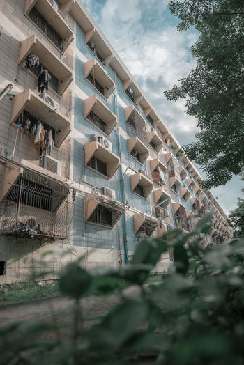 Low angle view of building and trees against cloudy sky