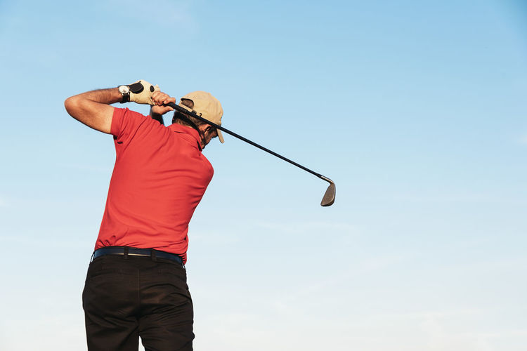 Rear view of man playing with golf club against sky