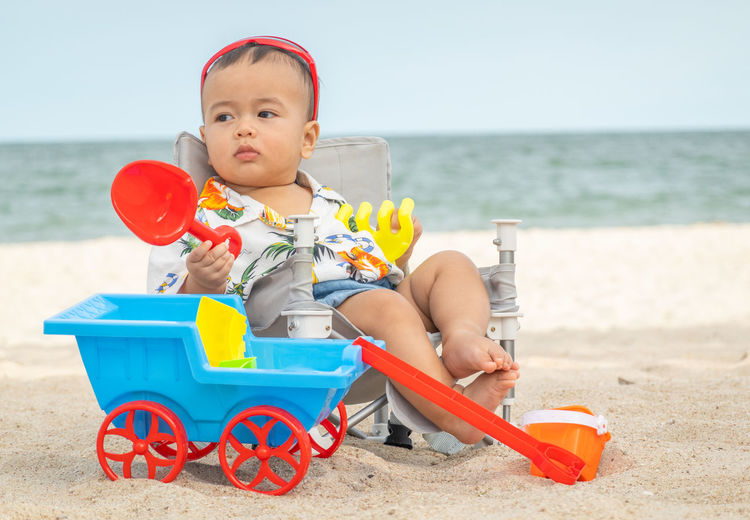 Cute baby girl sitting on toy at beach