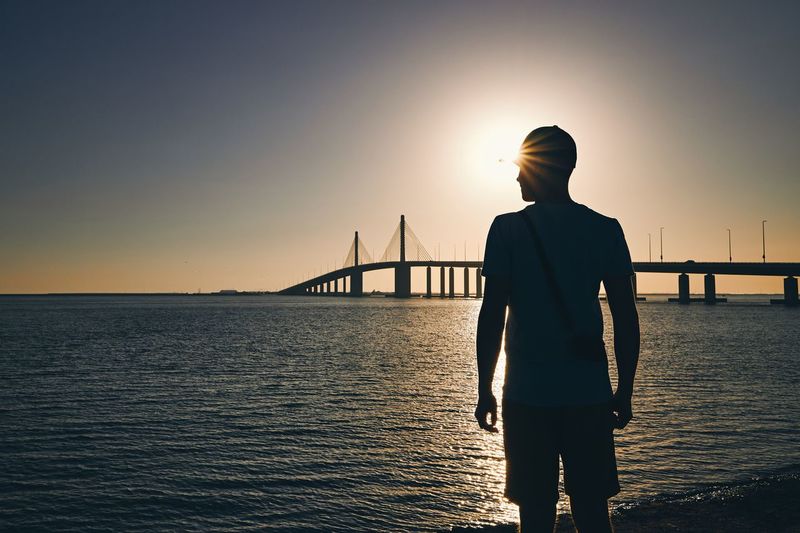 Rear view of silhouette man standing on bridge over sea against sky