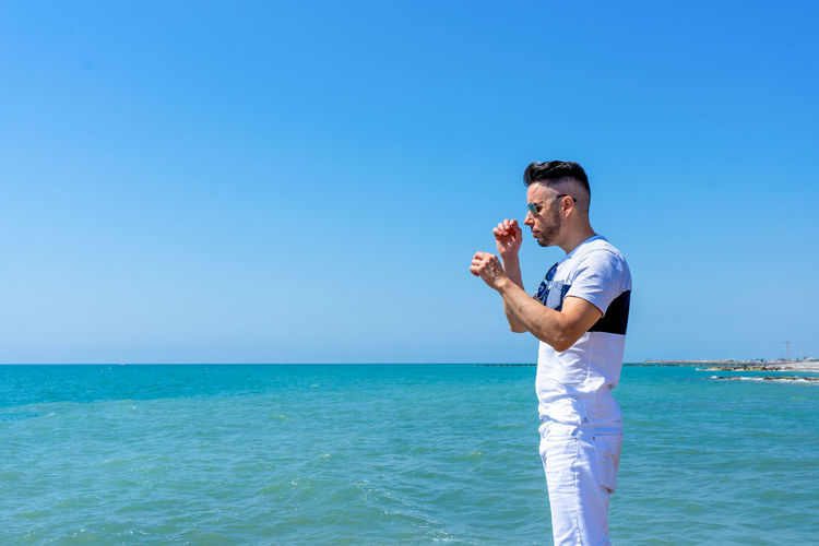 Side view of man standing at seashore against clear sky