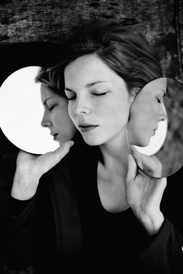 Close-up of woman with eyes closed holding mirrors with reflection