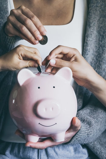 Hands putting coin in happy smiling piggy bank. saving money for household payments, bank bills.