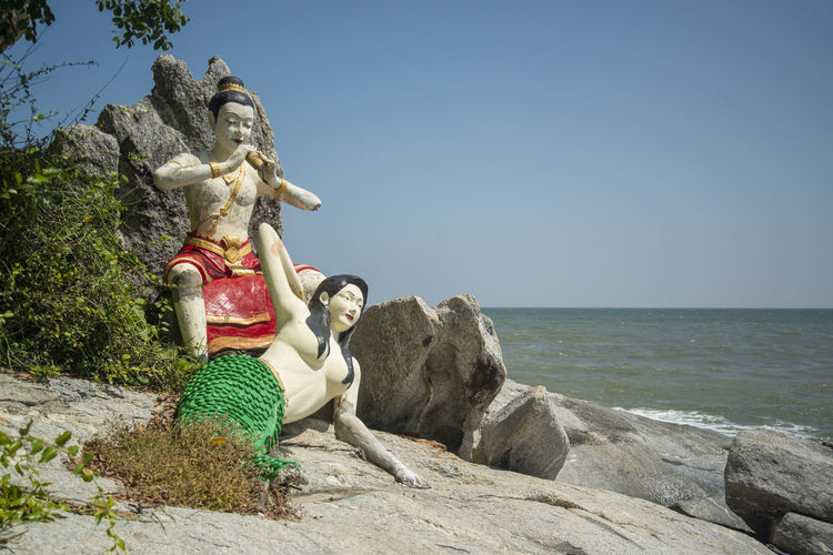 Side view of woman sitting on rock at beach