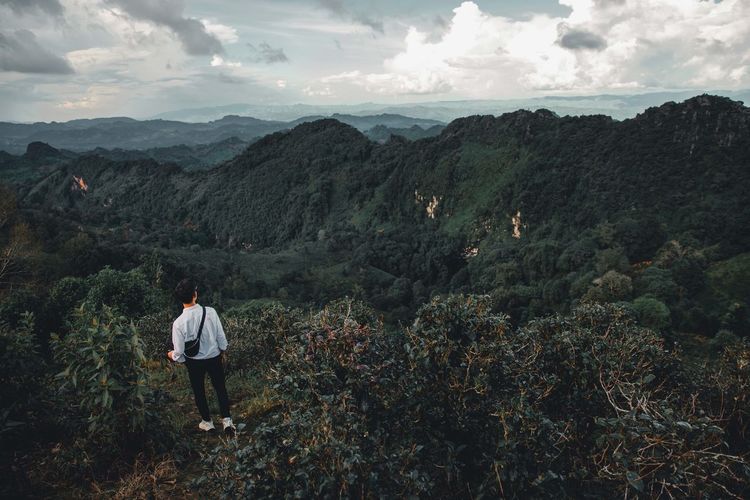 Rear view of man standing on mountain against sky