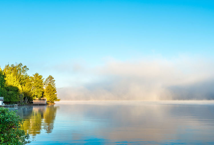 A summer early morning , colorful, mist clearing from a lake - a boathouse and dock in the distance