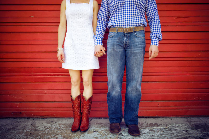 Low section of friends holding hands while standing against closed shutter