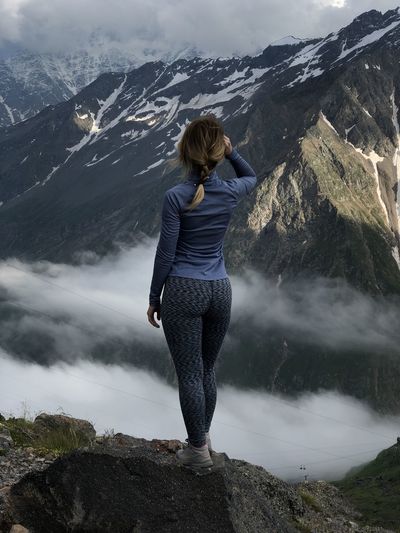 Rear view of woman standing on rock looking at mountain view