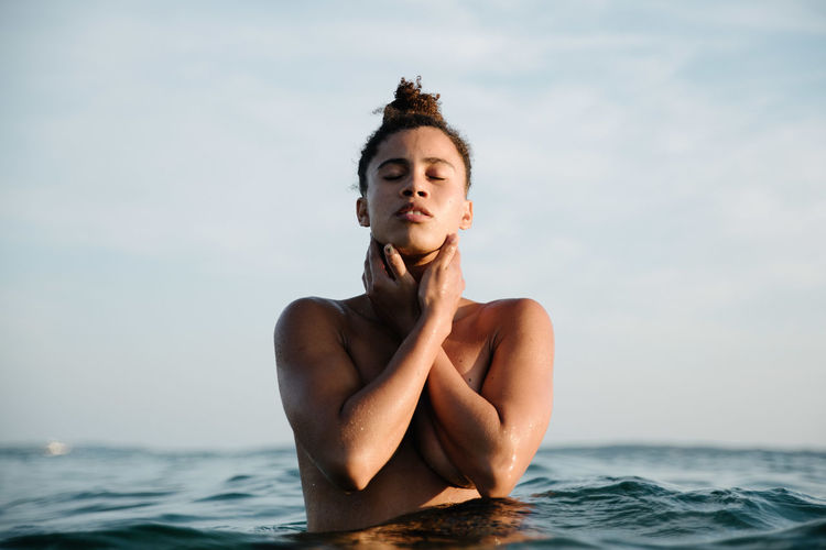 Shirtless woman in sea against sky during sunset