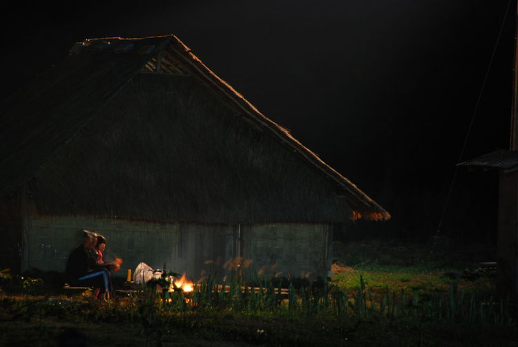 People sitting on grass by campfire at night against sky