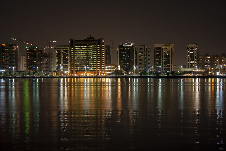 Illuminated buildings by river against sky at night in abu dhabi, united arab emirates