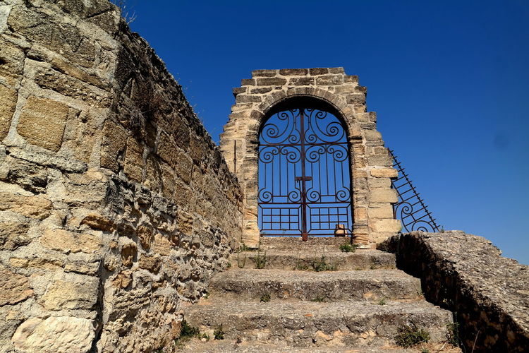 Low angle view of steps by closed gate against clear blue sky