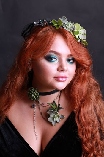 Portrait of sensuous young woman wearing wreath and necklace against black background
