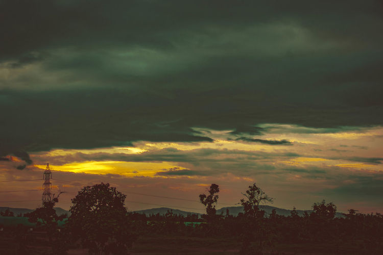 Silhouette trees against dramatic sky during sunset