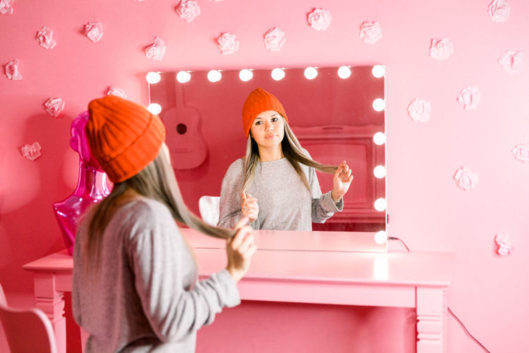 Young woman combing her hair in front of a mirror in a pink room