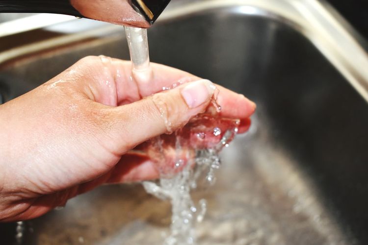 Cropped image of person hand with faucet in water at home