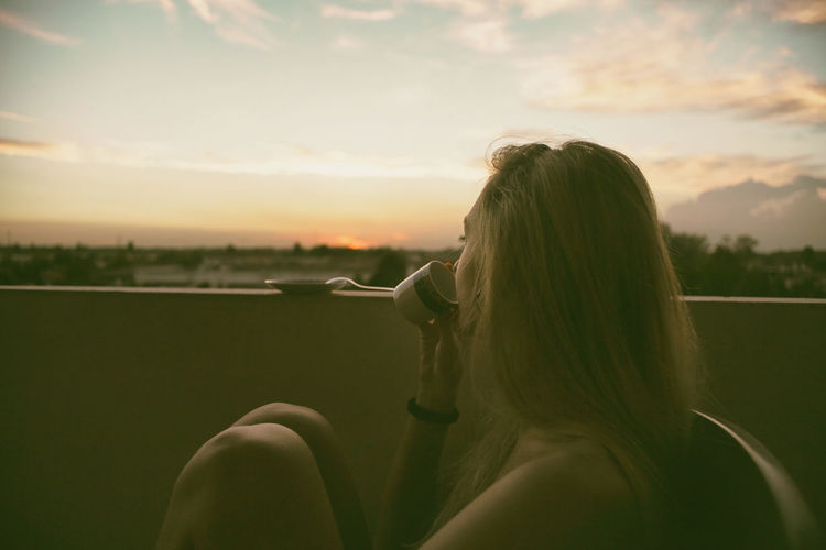 Side view of teenage girl having drink while sitting at balcony