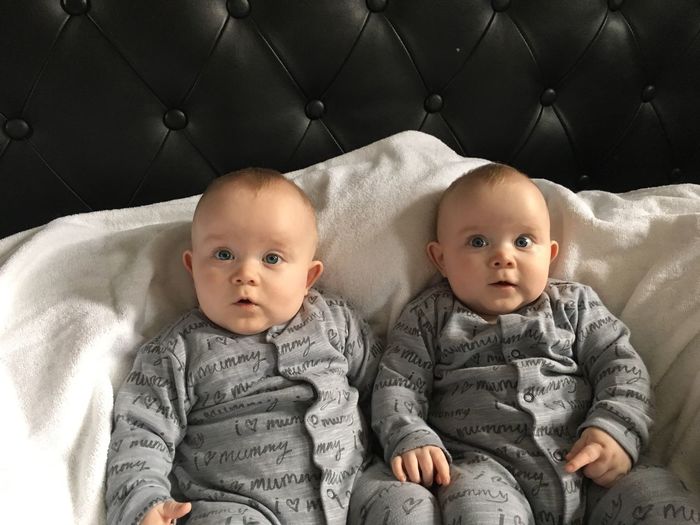 Portrait of cute twin baby boys sitting on bed