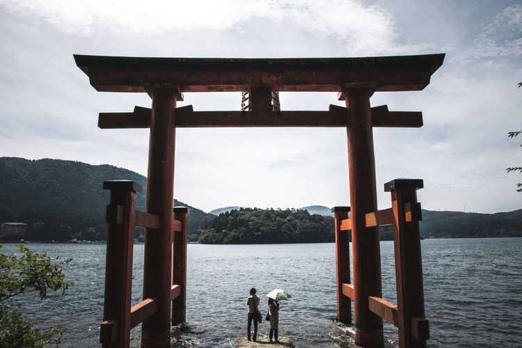 People standing by lake against sky