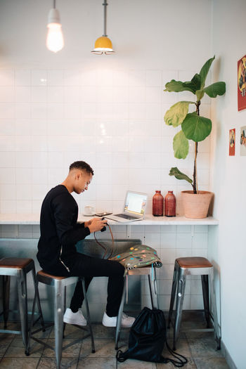 SIDE VIEW OF YOUNG MAN SITTING ON TABLE IN CAFE