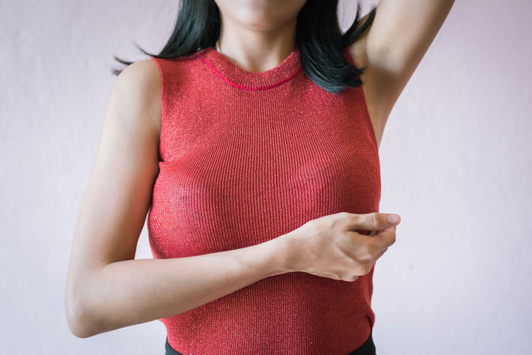 Midsection of woman touching breast while suffering from cancer while standing against white background
