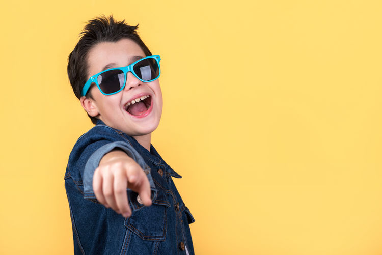 Boy wearing sunglasses standing against yellow background