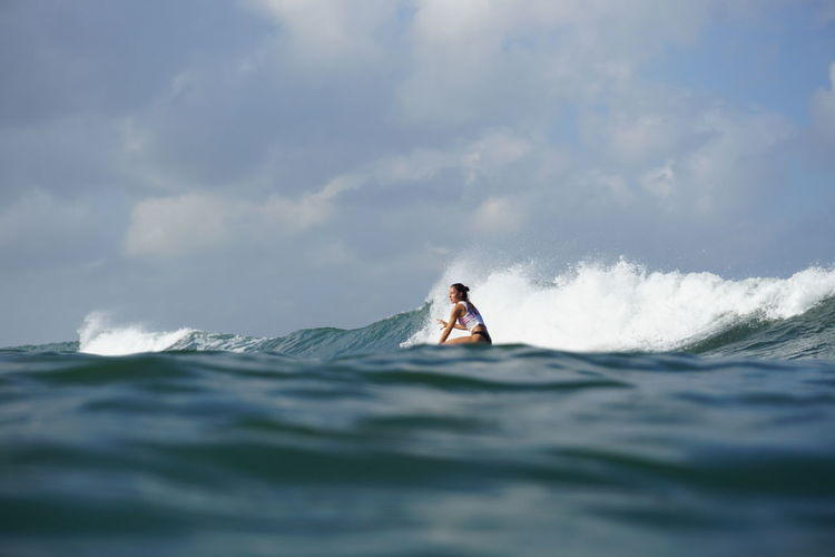 Side view of woman surfing in sea against sky