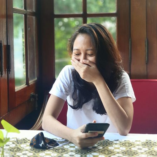 Asian young woman using phone while sitting on table in the restaurant 