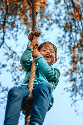 Low angle view of boy swinging against trees