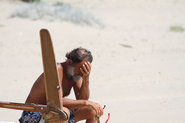 Shirtless man with head in hand sitting at beach
