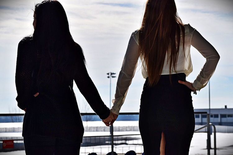Rear view of friends holding hands while standing by railing