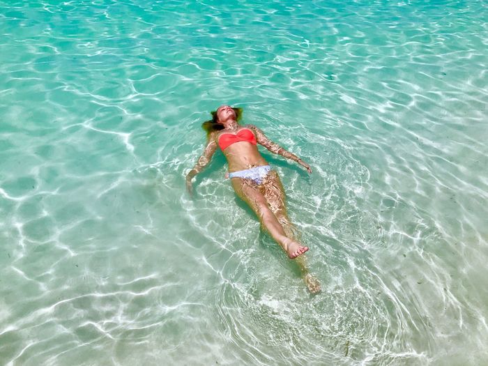 High angle view of woman in bikini lying in sea