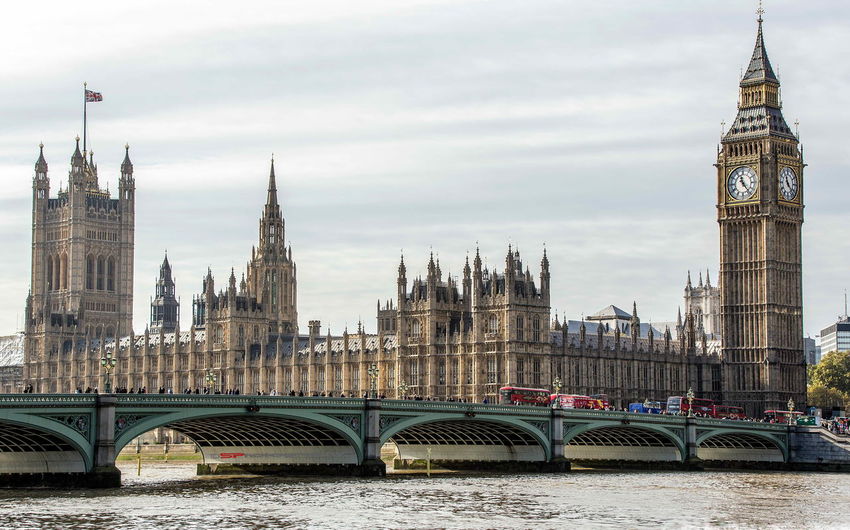 Westminster bridge over thames river by big ben and houses of parliament against sky