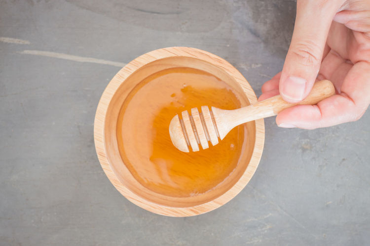 Cropped hand with honey in wooden bowl on table