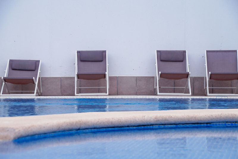 Empty chairs by swimming pool against wall