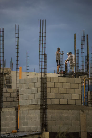 Low angle view of men working on building against sky